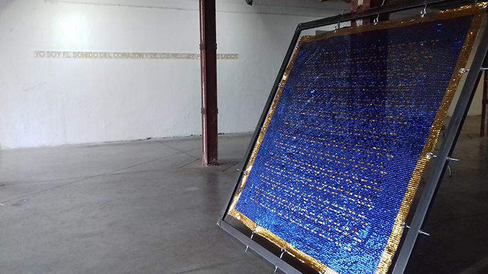 Sin "Título/Penar", de Román es un objeto/pintura/tapiz, hecha de lentejuelas azules y doradas pegadas a un pvc transparente que está sostenida a un marco de fierro a través de pernos.