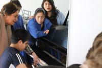 La Decana Clara Luz Cárdenas junto a los estudiantes de la Escuela Vista Hermosa, enseñándoles sobre el piano (Fotografía: Sergio Trabucco).